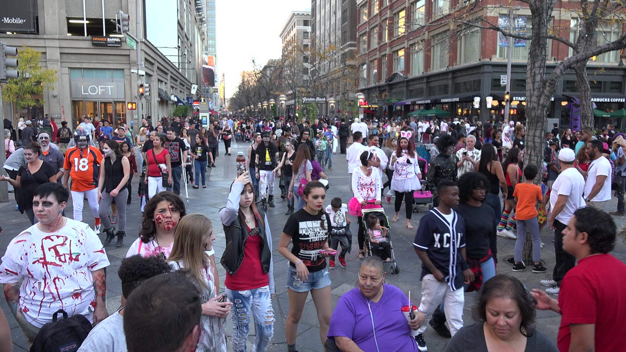 Crowded city sidewalk with costumed pedestrians and storefronts.