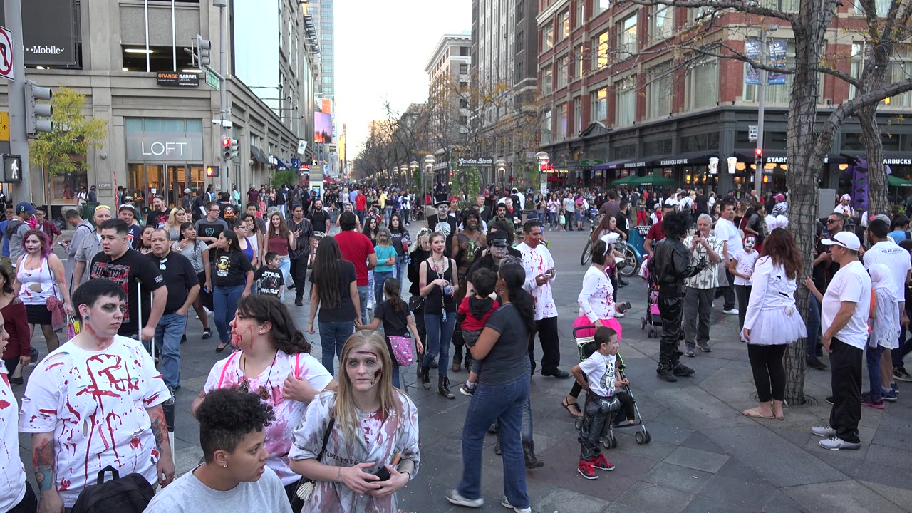 Downtown crowd with families, costumes, and commercial buildings.