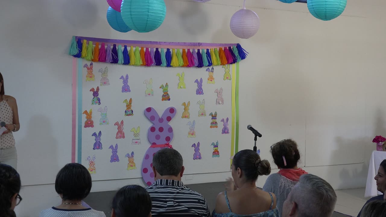 Audience faces a decorated Easter presentation wall with a microphone stand.