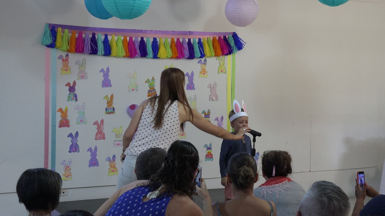 Woman adjusts a child at a microphone during a school performance.