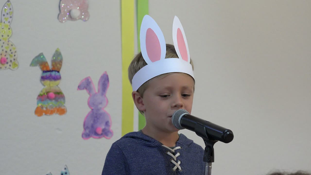 One second in, the boy in Cabo San Lucas looks downward while standing beside the black microphone and handmade bunny wall decorations.