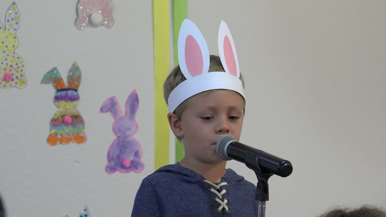 Young boy in bunny ears speaking into a microphone.