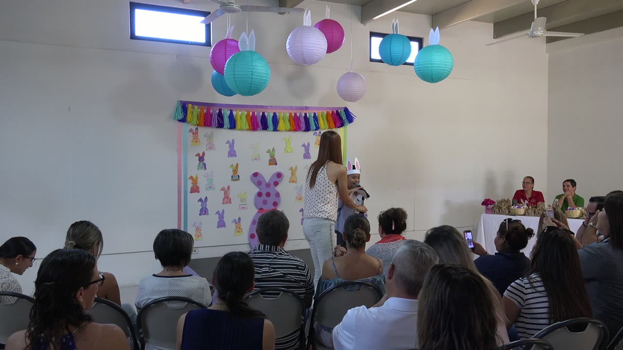 Audience watches a child at a microphone on a decorated stage.