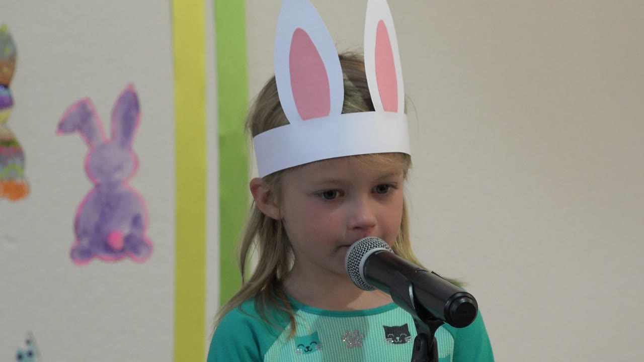 Young girl in bunny ears speaks into a microphone.
