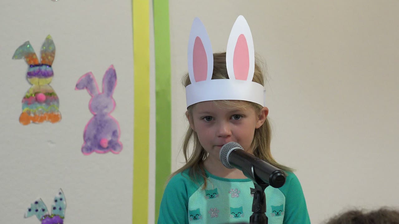 Girl in bunny ears looking forward behind a microphone.