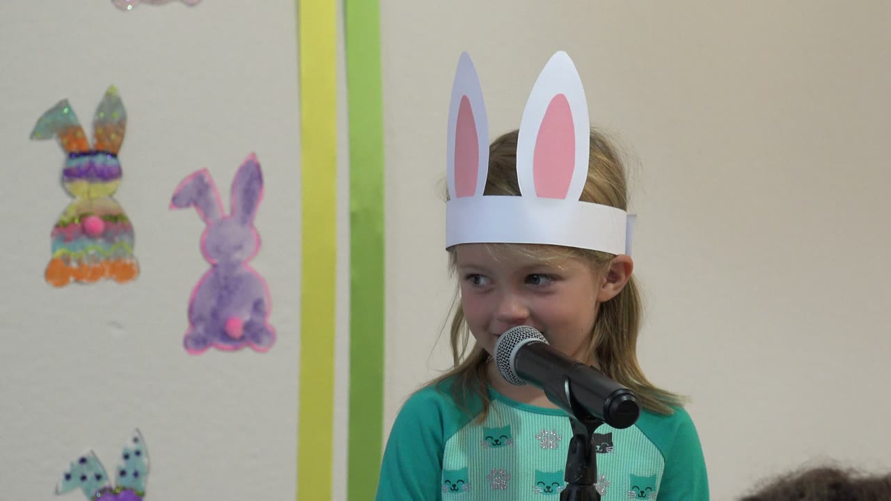 Young girl in bunny ears stands at a microphone.