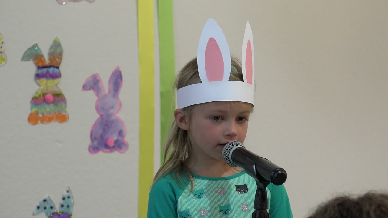 The girl in Cabo San Lucas looks down toward the microphone, with her rabbit-ear headband centered and painted bunny decorations visible on the wall.