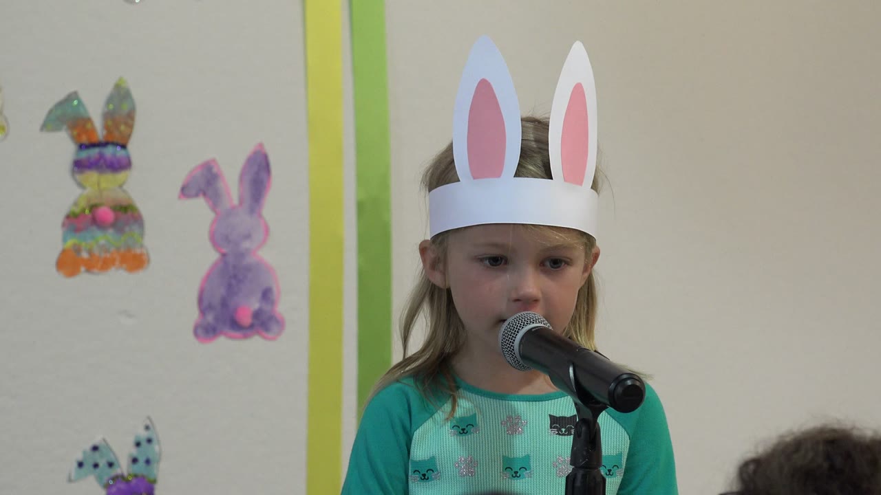 Young girl in bunny ears speaking into a microphone.