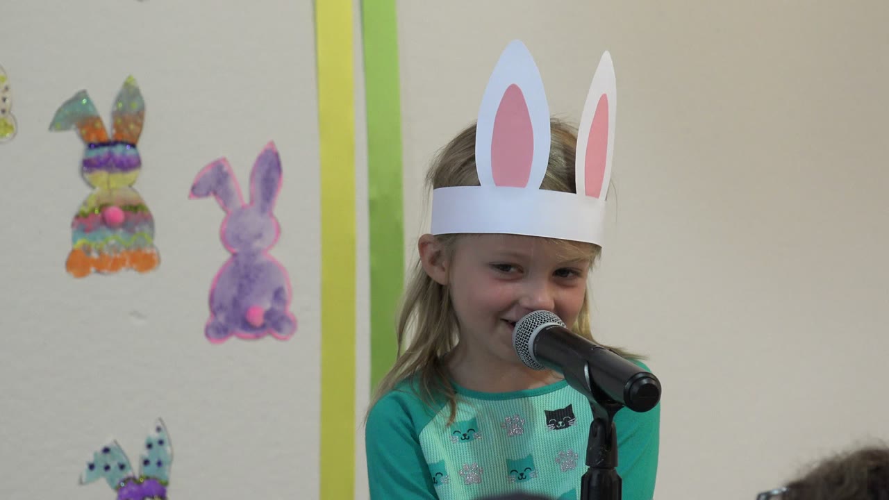 Young girl in bunny ears speaking into a microphone.