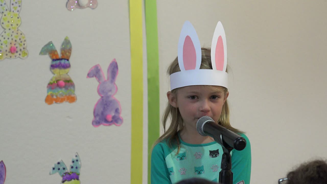In Cabo San Lucas, Mexico, the girl faces forward at the microphone, with pastel paper rabbits and vertical green wall trim visible around her.