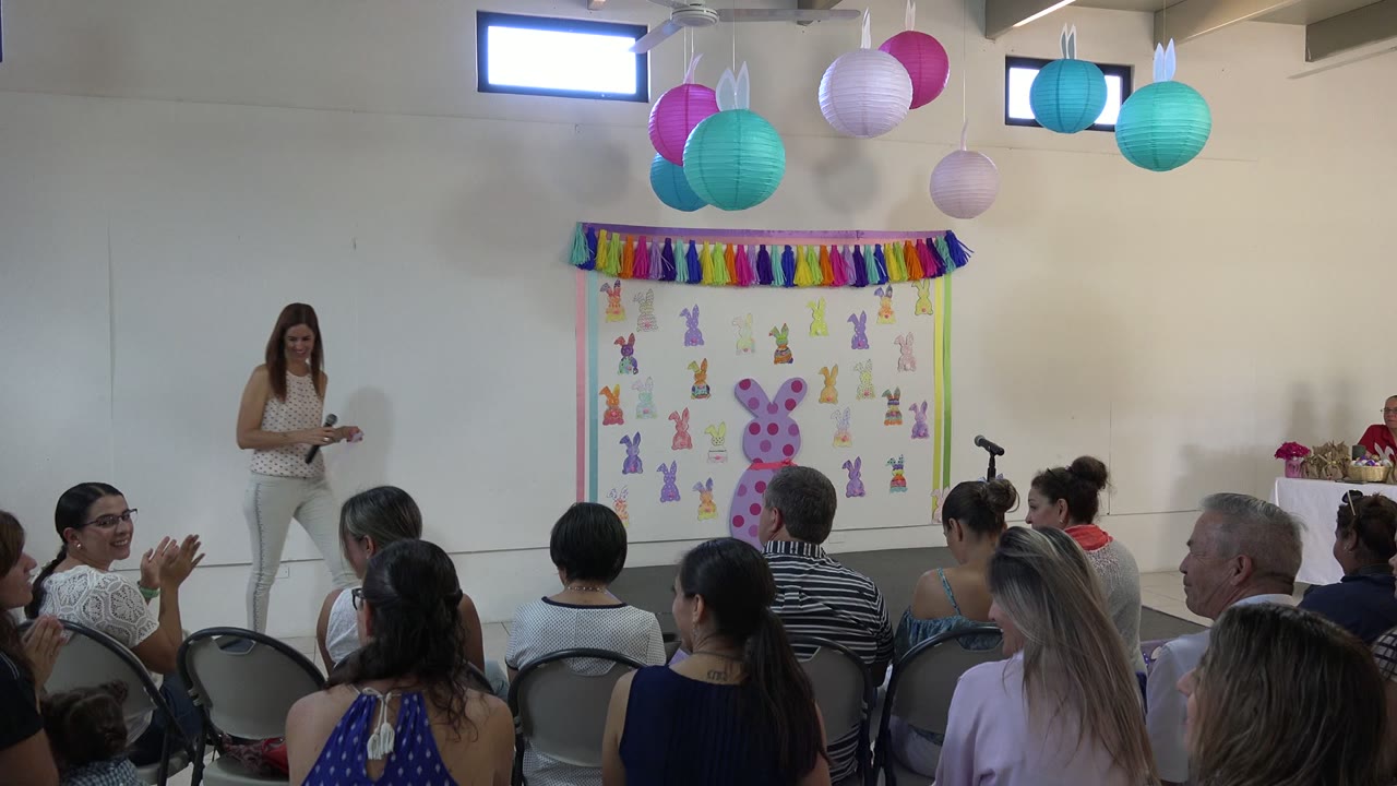 Young woman standing near a decorated stage in front of a seated audience.
