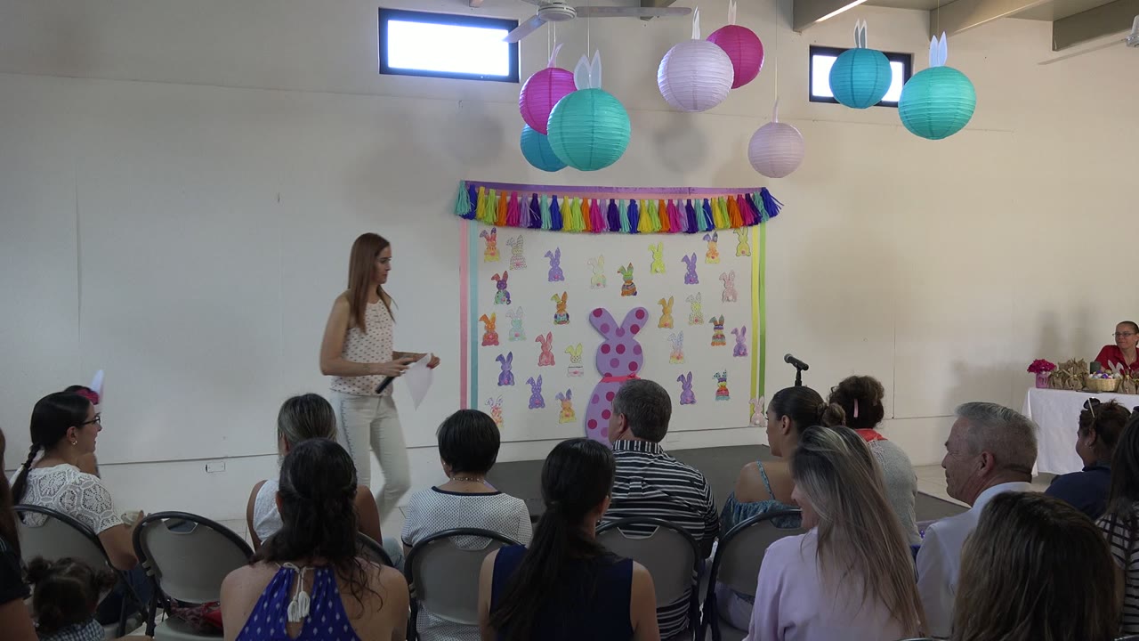 A woman moves across the front of the Cabo San Lucas event room while the seated audience faces the bunny backdrop and microphone stand.