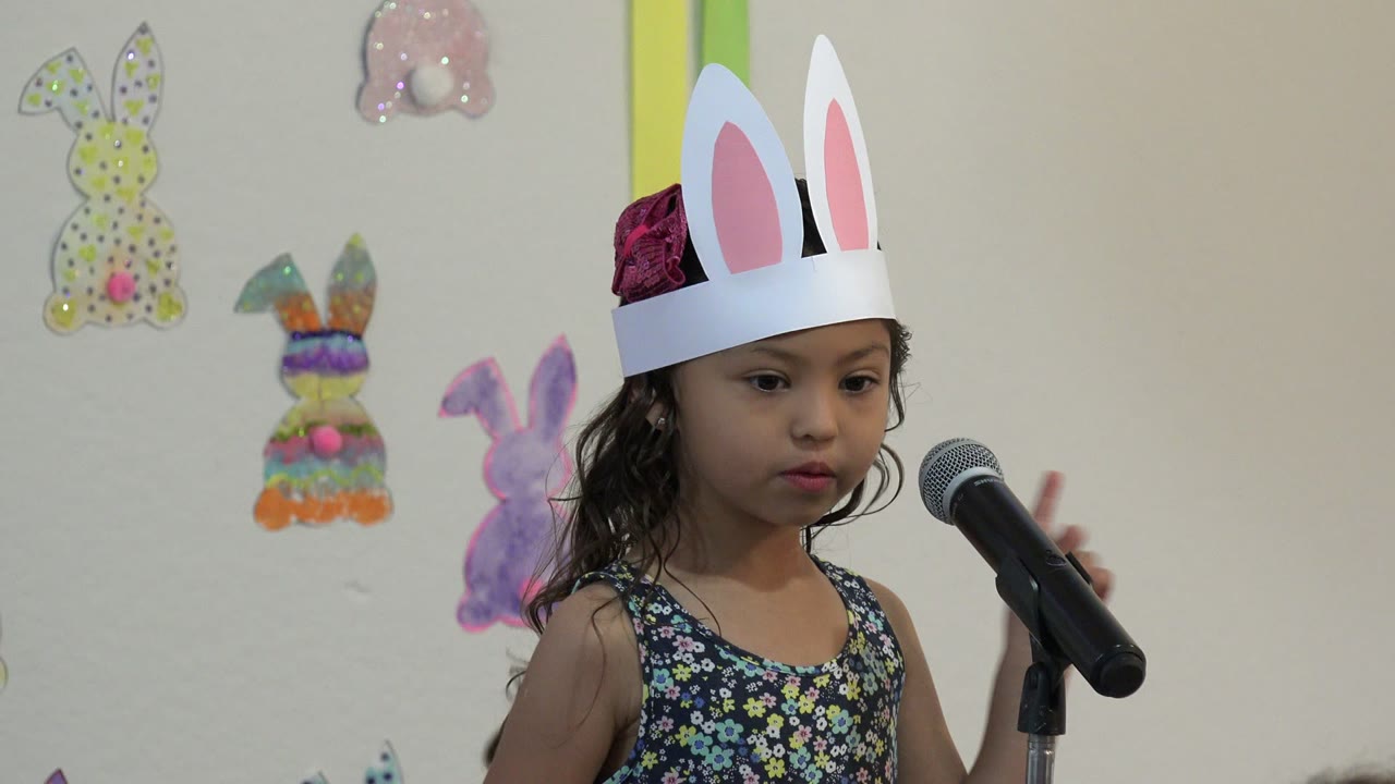 In Cabo San Lucas, Mexico, the girl in white rabbit ears faces the microphone with her mouth slightly pursed and one hand raised beside the mic.
