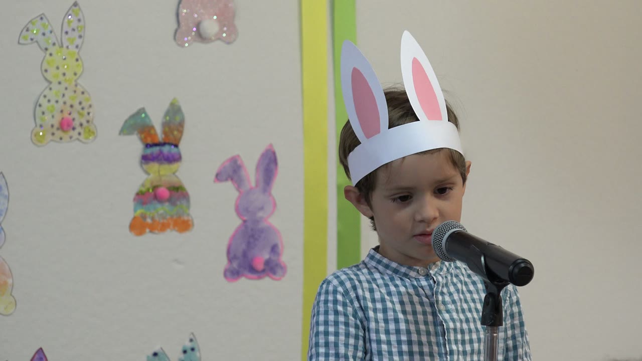 Young boy wearing paper rabbit ears stands at a microphone.