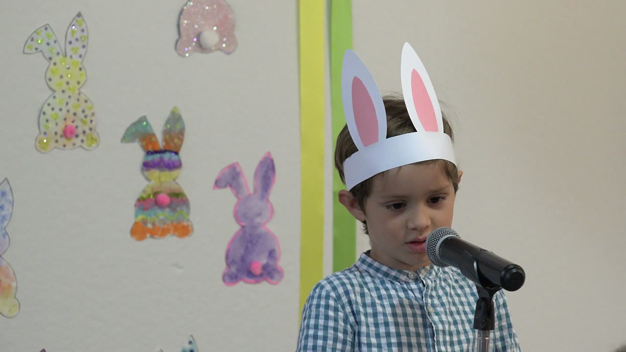 At 0:01, the boy leans slightly toward the microphone while wearing paper rabbit ears, with colorful handmade bunny cutouts visible on the wall in Cabo San Lucas, Mexico.