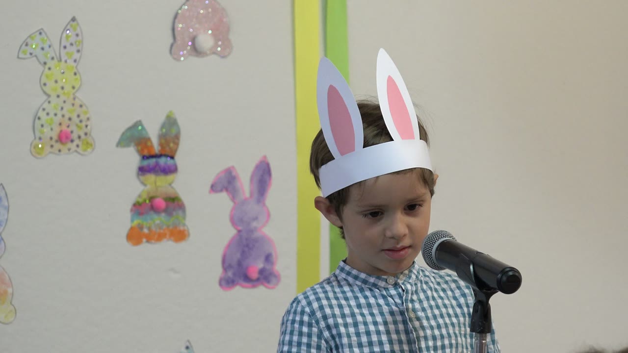 Young boy in bunny ears standing at a microphone.