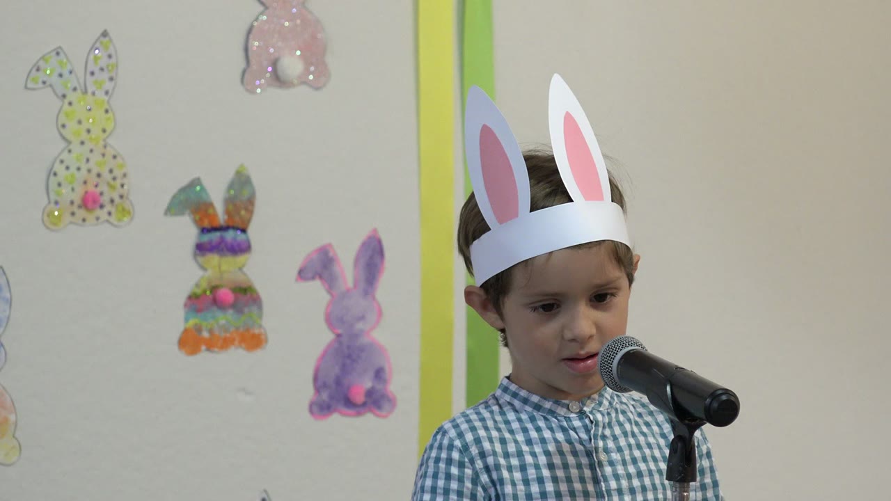 At 0:01, the boy looks slightly downward beside the microphone, with colorful rabbit decorations arranged on the wall in the Cabo San Lucas performance setting.