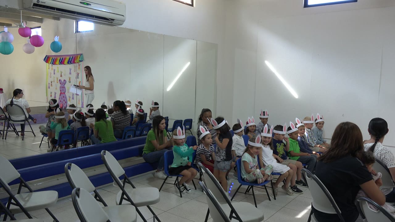 Children wearing bunny ears sit in rows during an indoor Easter event.