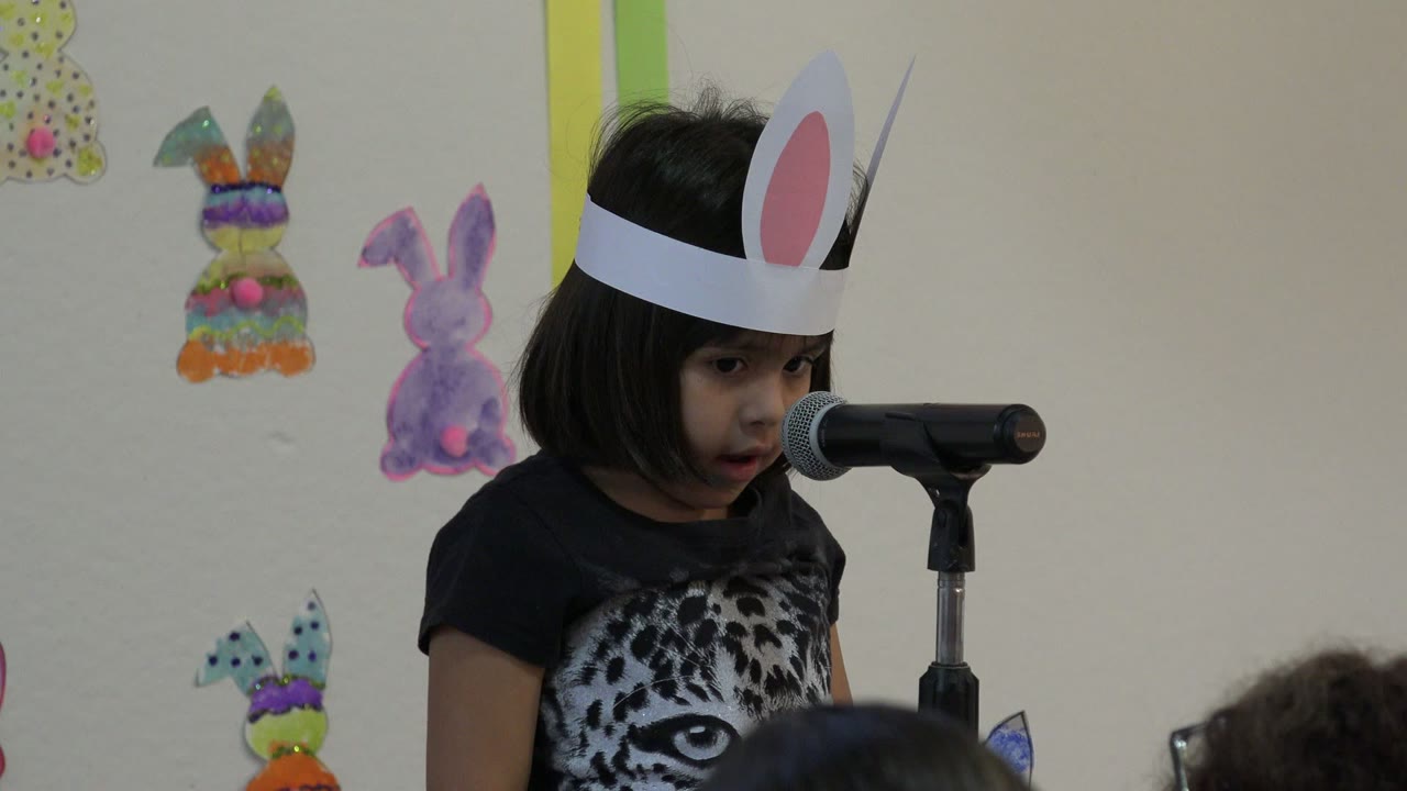 The child in Cabo San Lucas looks down slightly beside the microphone, with a white bunny-ear headband and handmade rabbit decorations visible behind her.