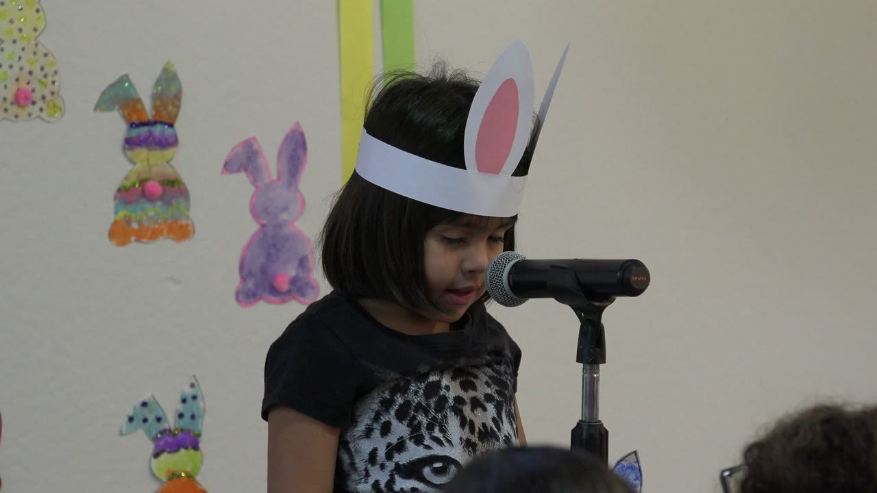 Girl in bunny ears near a microphone with rabbit decorations behind her.