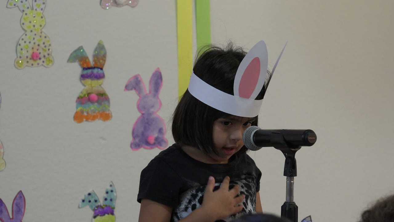 Young child in paper bunny ears speaking into a microphone.