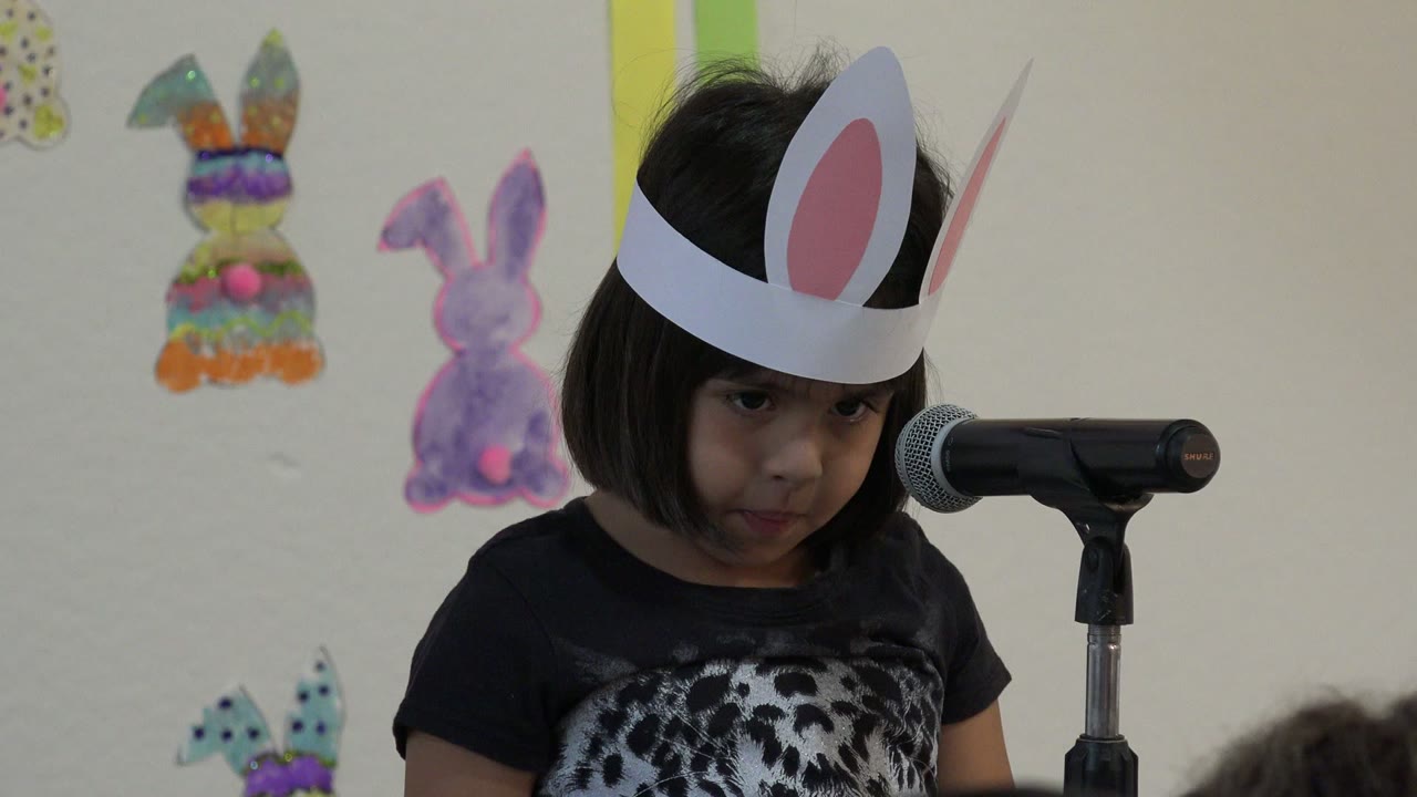 Child in bunny ears looking toward a microphone.