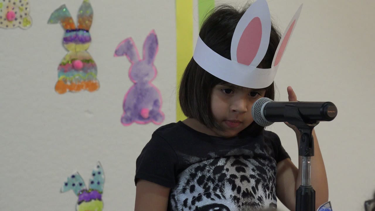 Child wearing bunny ears facing a microphone