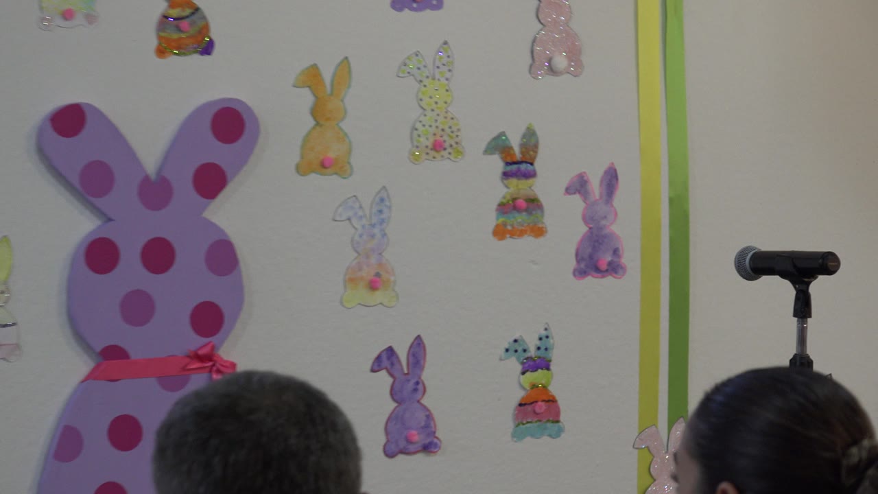 At 0:01 in Cabo San Lucas, Mexico, the frame holds on audience members in the foreground with a black microphone stand beside a large pink bunny decoration.