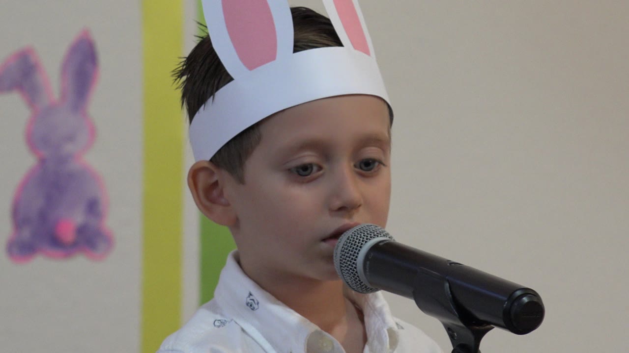 Young boy in bunny ears speaking into a microphone.