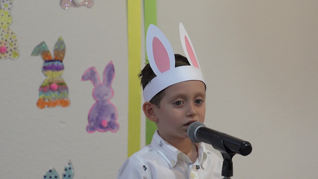 Boy stands at a microphone with Easter rabbit decorations in the background.