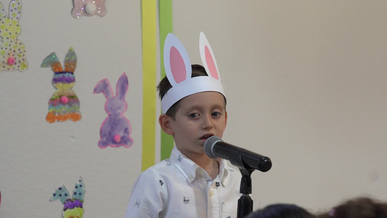 Young boy wearing paper bunny ears speaks into a microphone.