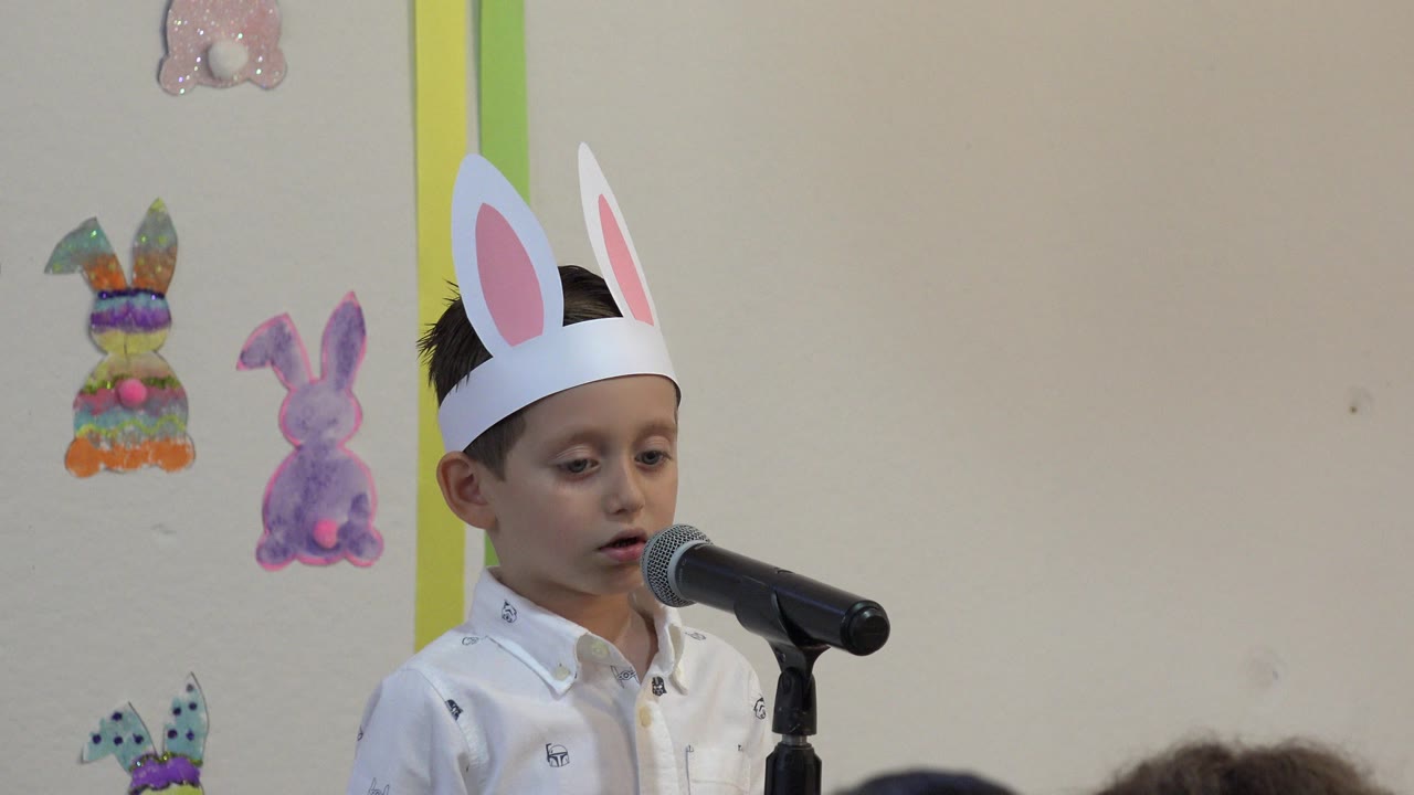 Young child in paper bunny ears standing at a microphone.