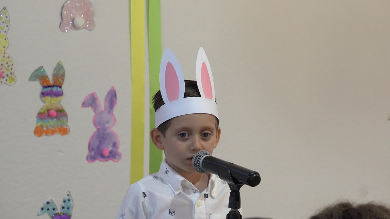 Boy in rabbit ears speaking into a microphone in front of rabbit decorations.