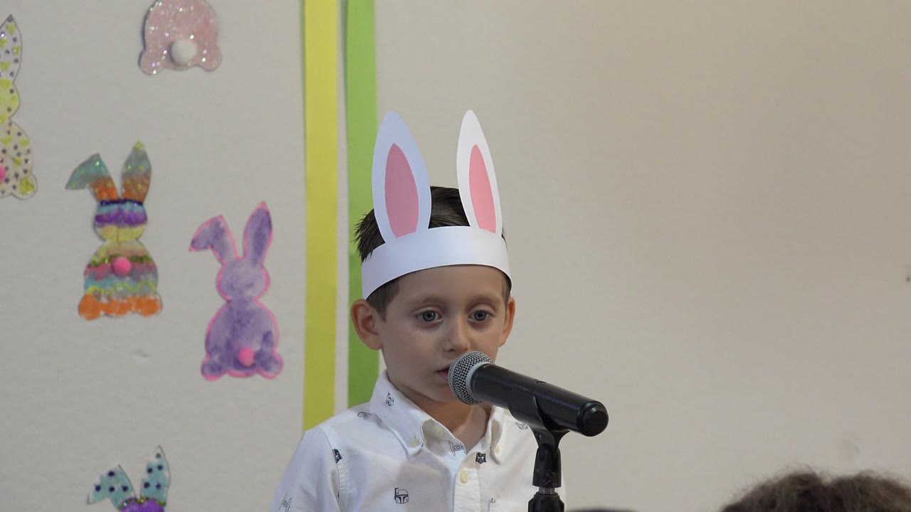 The boy remains near the microphone in Cabo San Lucas, Mexico, with colorful rabbit cutouts visible on the beige wall behind him.