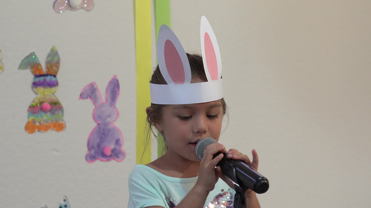 Girl in bunny ears looks down while holding a microphone.