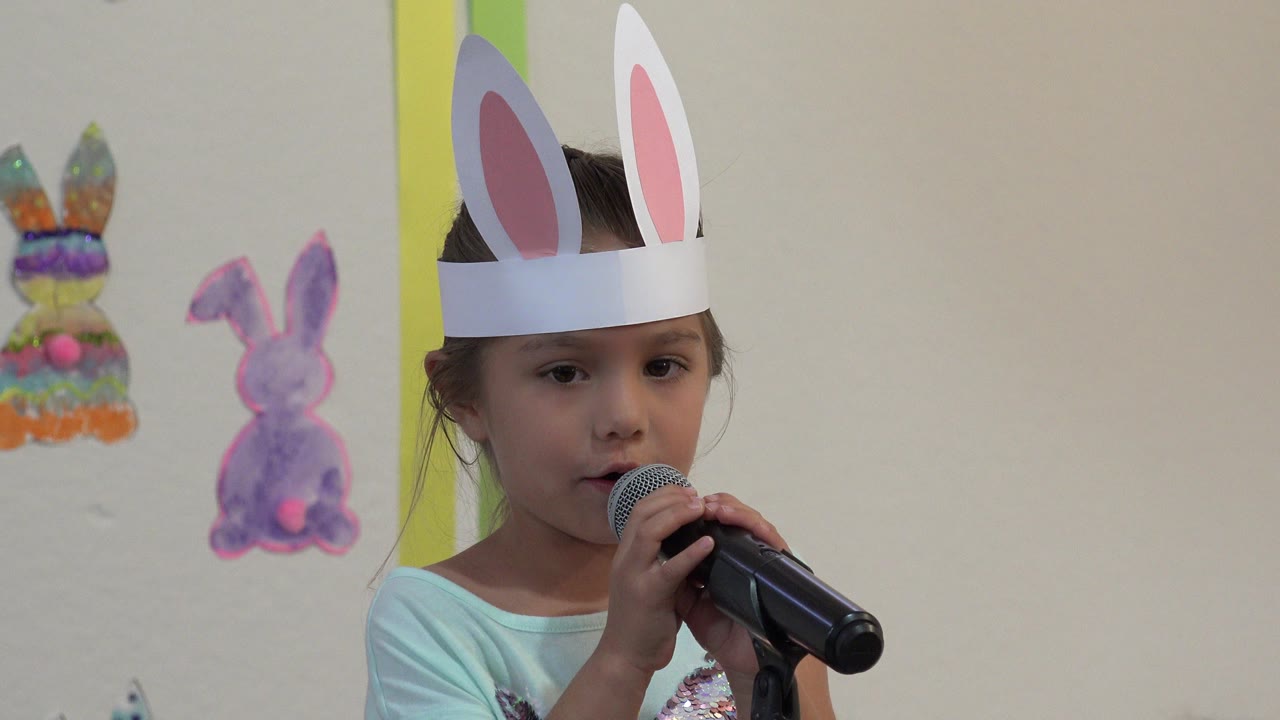 At the opening moment in Cabo San Lucas, Mexico, a young girl in handmade bunny ears faces forward while holding a black microphone below her mouth.