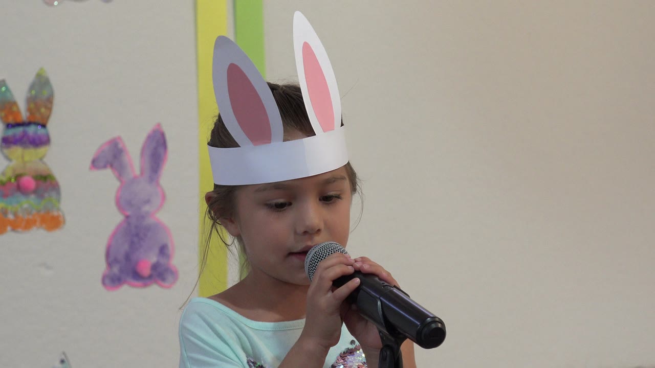 Girl in bunny-ear headband looking down while holding a microphone.