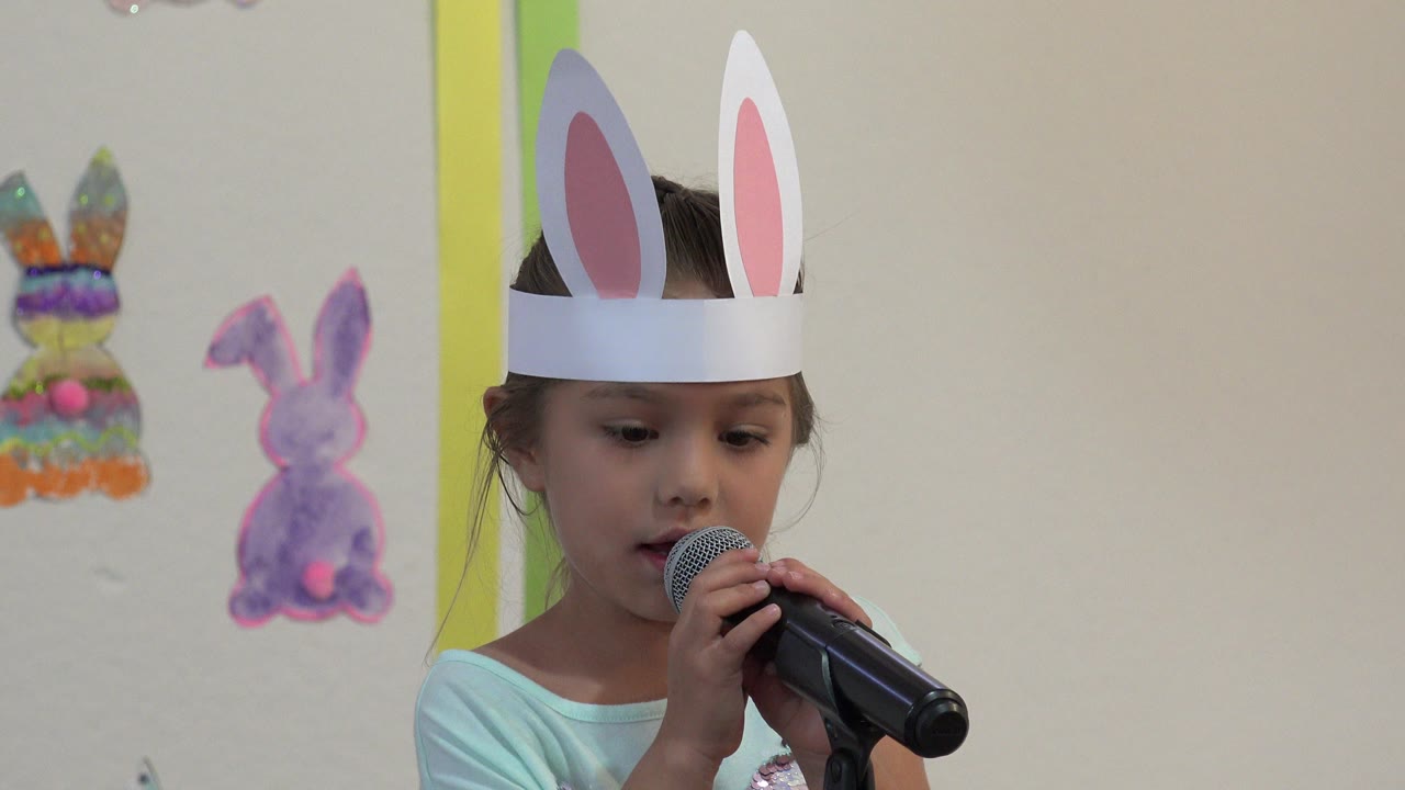 The girl keeps the microphone close to her mouth, with two pastel bunny decorations visible on the wall behind her in Cabo San Lucas, Mexico.