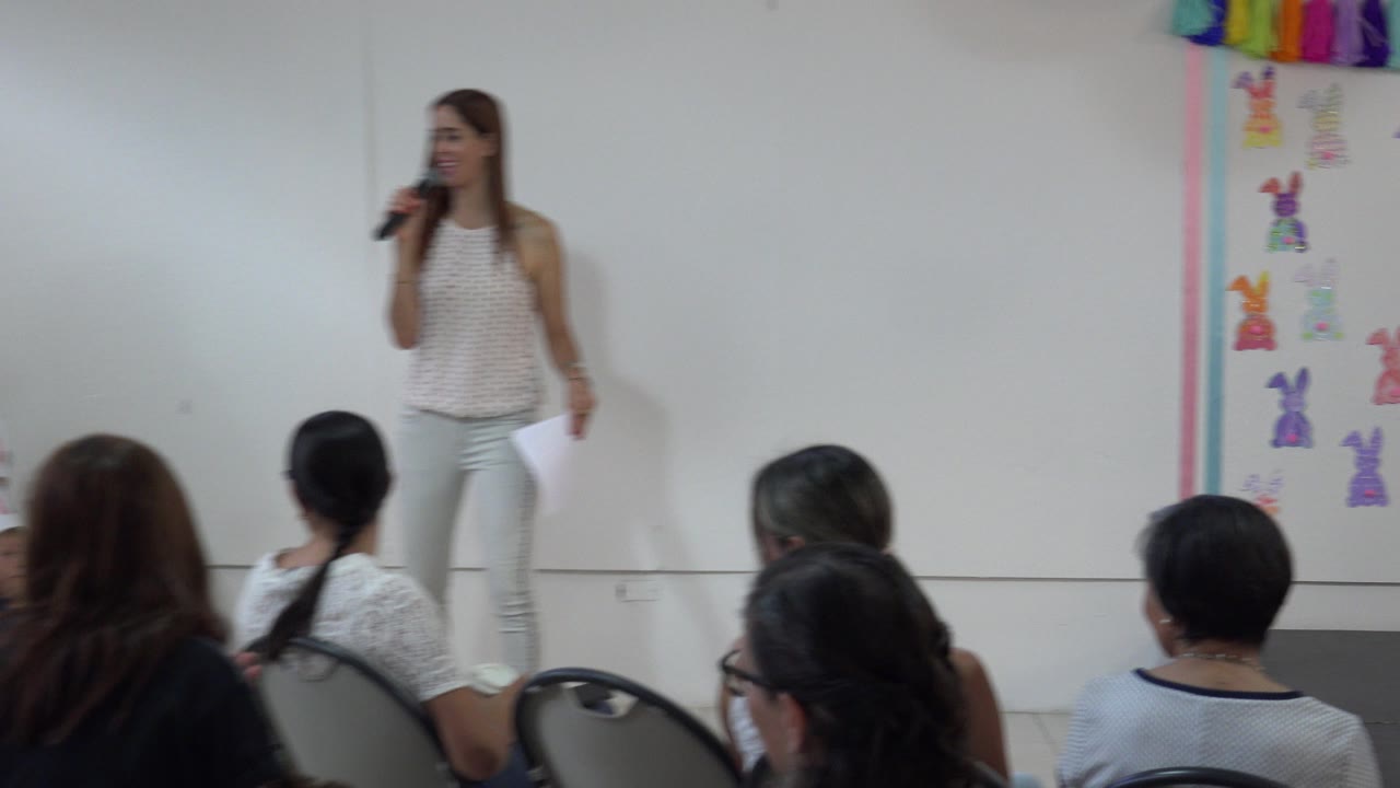 Teacher holding a microphone in front of seated adults in a classroom.