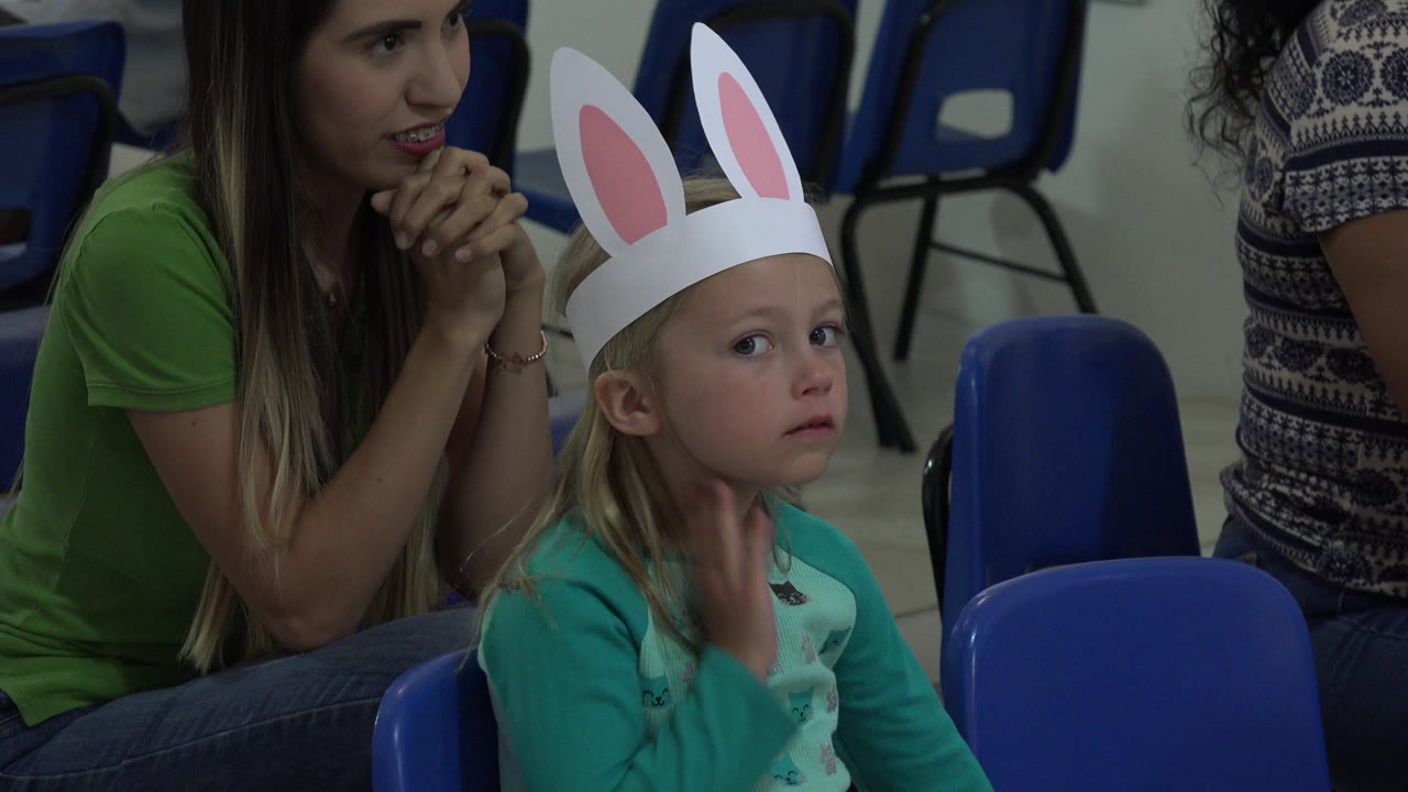 Young girl in bunny ears sits beside an adult woman on blue chairs.