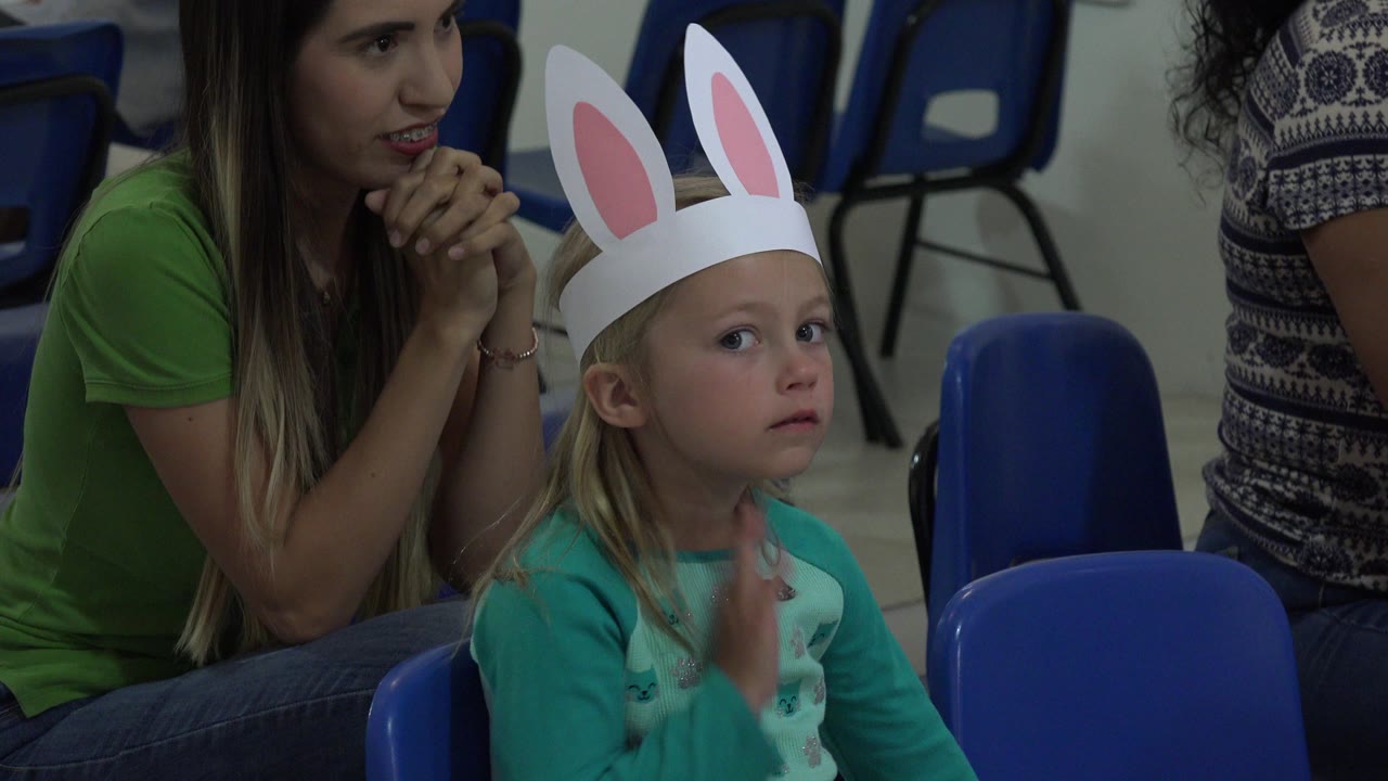 One second into the Cabo San Lucas footage, the child in paper bunny ears lifts her hand near her chest while seated among blue plastic chairs.