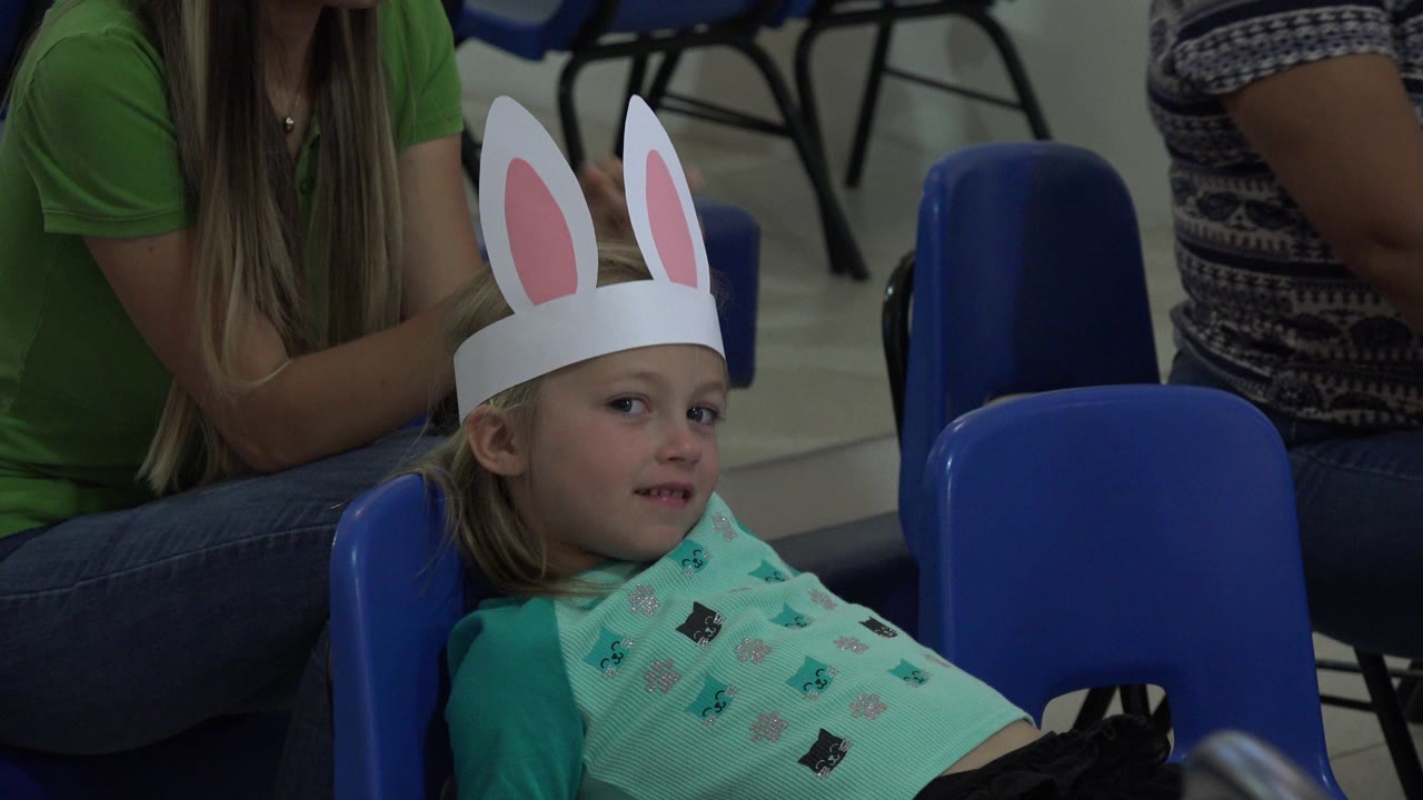 Young girl in rabbit ears sitting on a blue chair indoors.