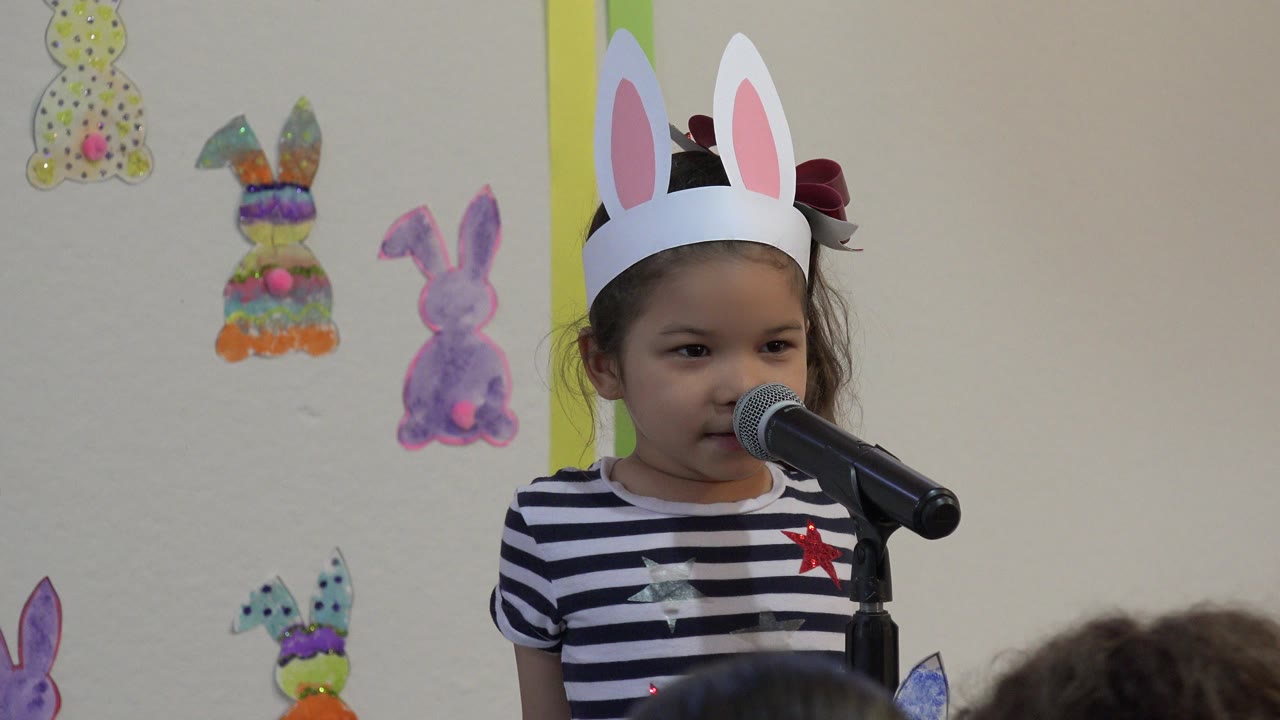 Young girl in paper bunny ears standing at a microphone.
