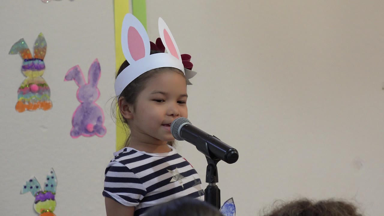Young girl wearing paper bunny ears speaks into a microphone.