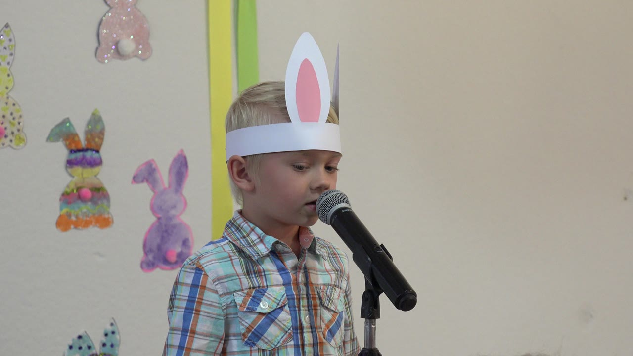 Young boy in bunny ears speaking into a microphone.