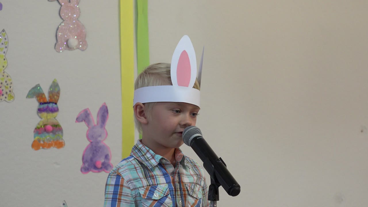 Young boy wearing paper bunny ears speaks into a microphone.