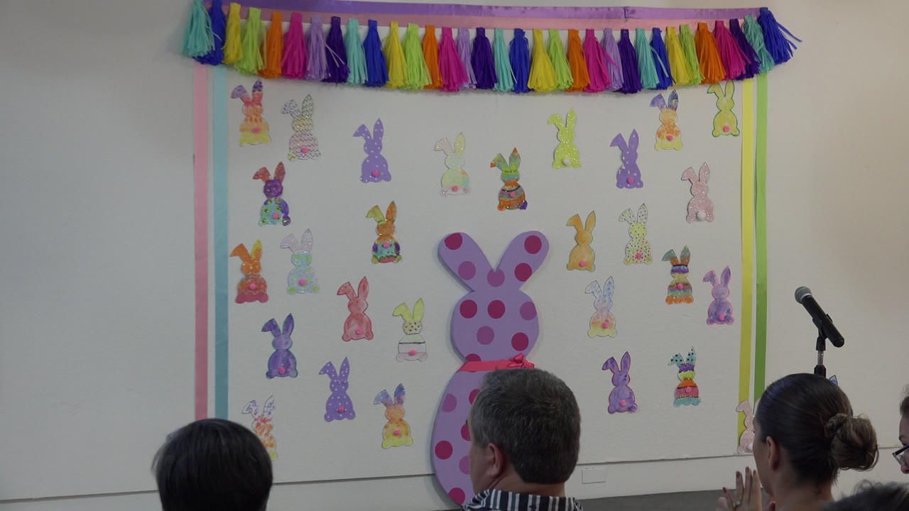 Decorated classroom wall with audience heads and a microphone stand.