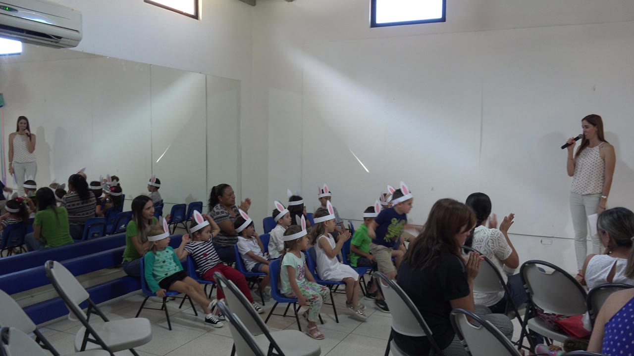 Presenter with microphone facing seated children in bunny ears