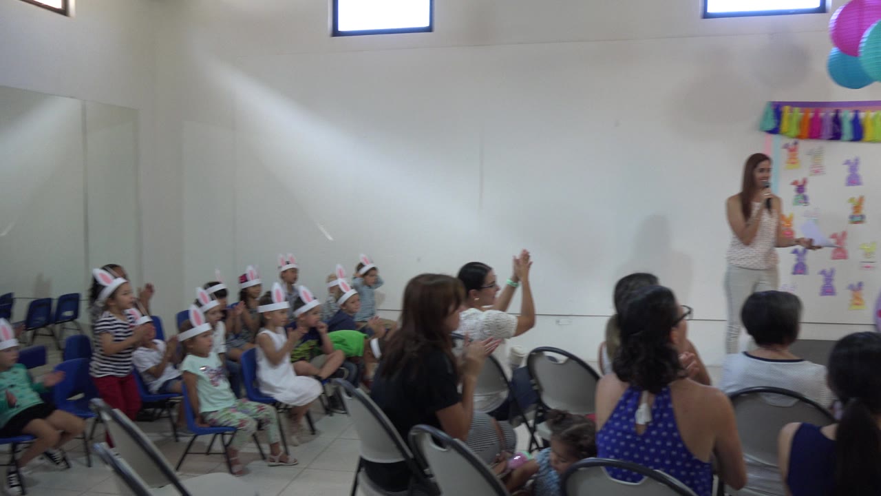 Audience seated in a decorated school room while a woman speaks near the front.
