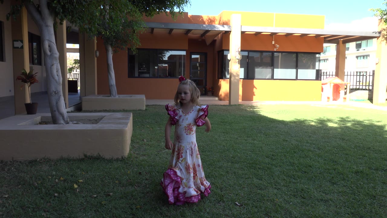 Young girl on grass near a tan and orange building.